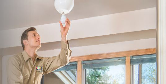 Home Energy Squad member installs LED lightbulb