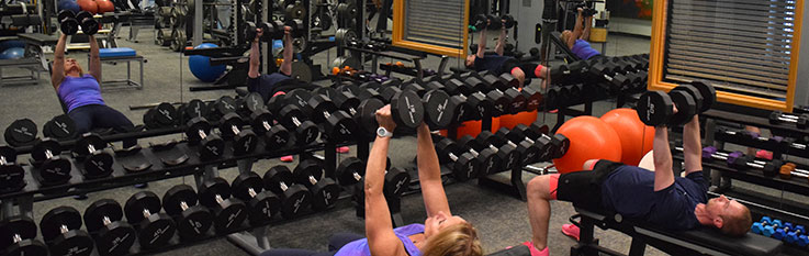 Two people lifting free weights in front of mirror