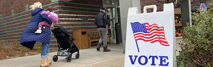 People walking into building behind Vote Here sign