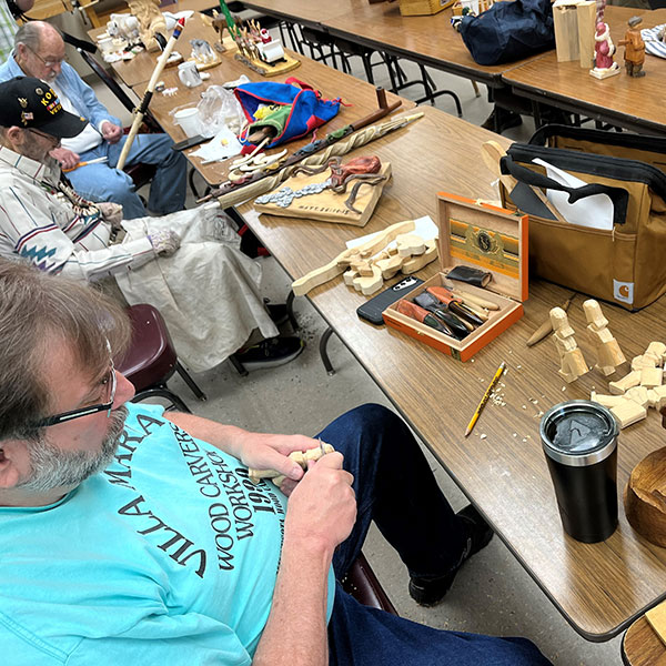 Three men carving wood with tools on table