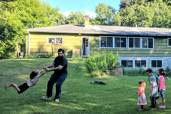 Man twirling little girl in front of green house