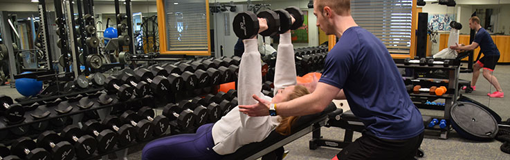 Man spot lifting for a woman with dumbbells