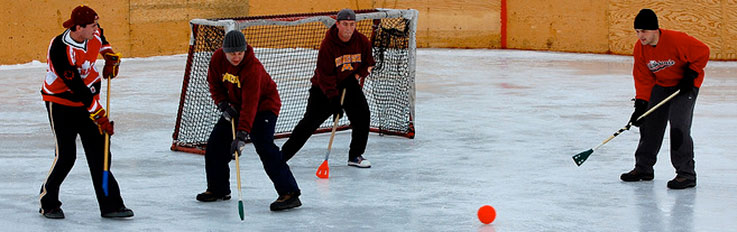 Four men wearing boots on ice with sticks and ball