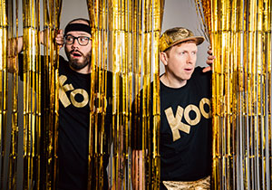 Two men dressed in black behind a gold curtain