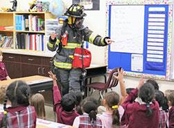 Firefighter in gear surrounded by kids in classroom