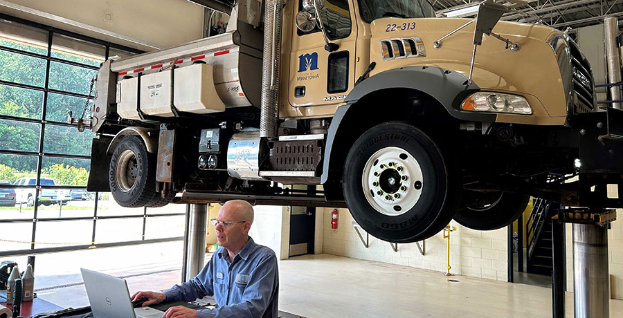 Man sitting at computer in front of large truck on lift